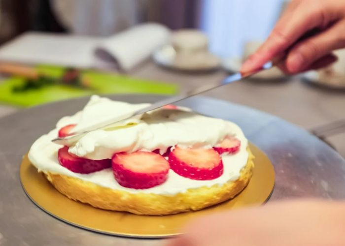 A strawberry shortcake is being made at a cooking class in Tokyo, where a palette knife is being used to spread cream over strawberries.